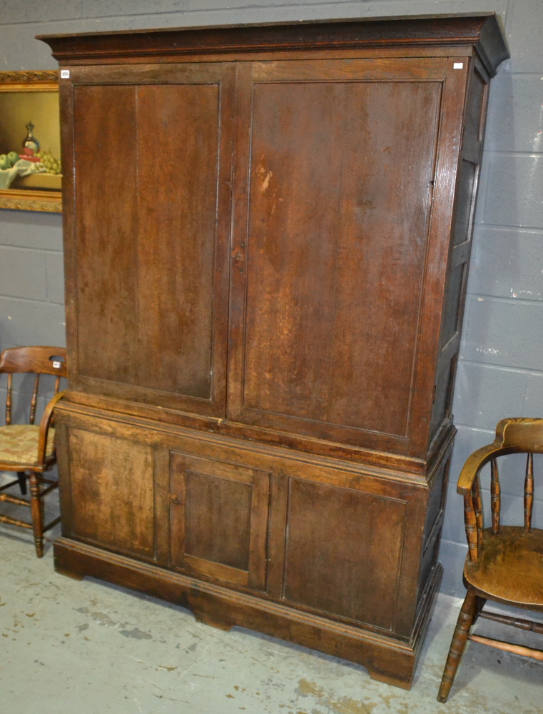 An early 19th Century oak linen cupboard enclosed by a pair of panel doors over a cupboard plinth