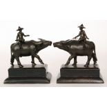 A pair of early 20th Century Burmese bronze figures of peasants each wearing a hat and sat astride