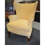 Revised estimate - An early 20th Century wingback armchair with yellow fabric upholstery,