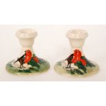 A pair of Moorcroft Pottery squat candlesticks each decorated with a robin perched amidst holly