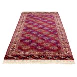 Persian Bokhara rug, decorated with colourful geometric medallions upon a red ground, 82" x 50"