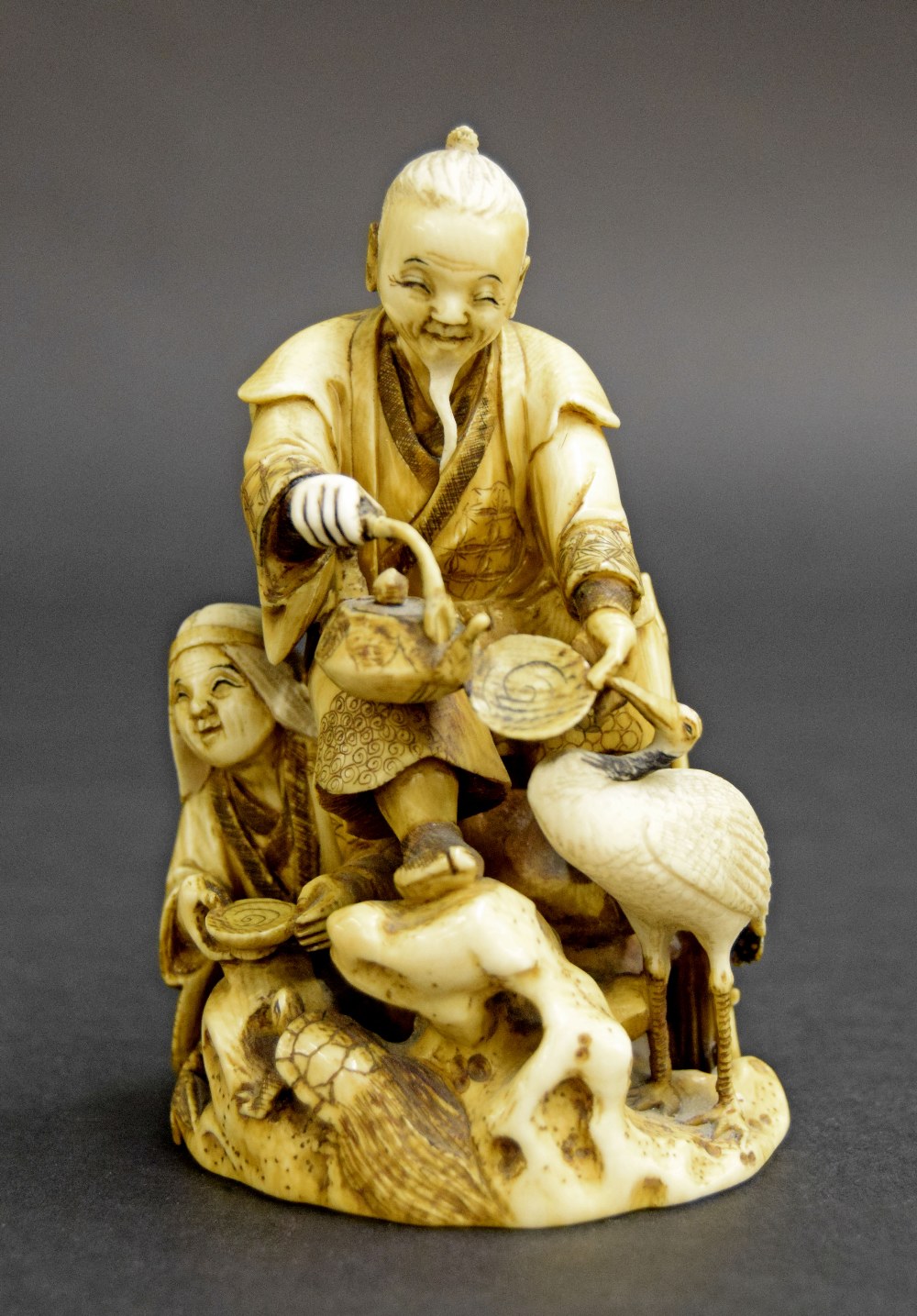 Japanese carved stained ivory okimono, modelled with two figures in a naturalistic setting holding