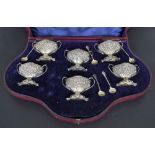 Fine Edwardian cased set of six silver twin handled salts and five matching spoons, repousse with