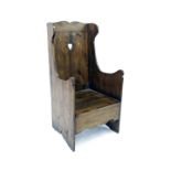 Antique oak lambing chair, the panelled back inset with a heart motif over a solid seat and shaped