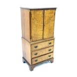Repica burr walnut tallboy, with double doors enclosing glass shelves over three drawers upon