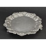 Edward VII circular silver salver with a moulded shell and scroll foliate border upon three paw