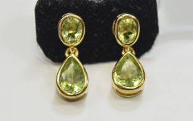 Pair of Peridot Drop Earrings, a pear cut suspended below an oval cut of the bright,