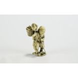 Ivory Figural Netsuke, showing a man walking along with a staff, carrying a creature in a basket