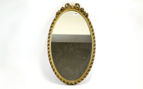 Mirror Oval mirror in dark gilt frame with central bow and floral moulding to top. Approx height 23.