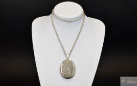 A Large Oval Shaped Hinged Locket With Engraved Decoration And Attached Long Silver Chain.