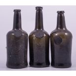 Three coloured glass bottles, each with an applied seal, F WOLLASTON, BURY SUFFOLK, 27cm.