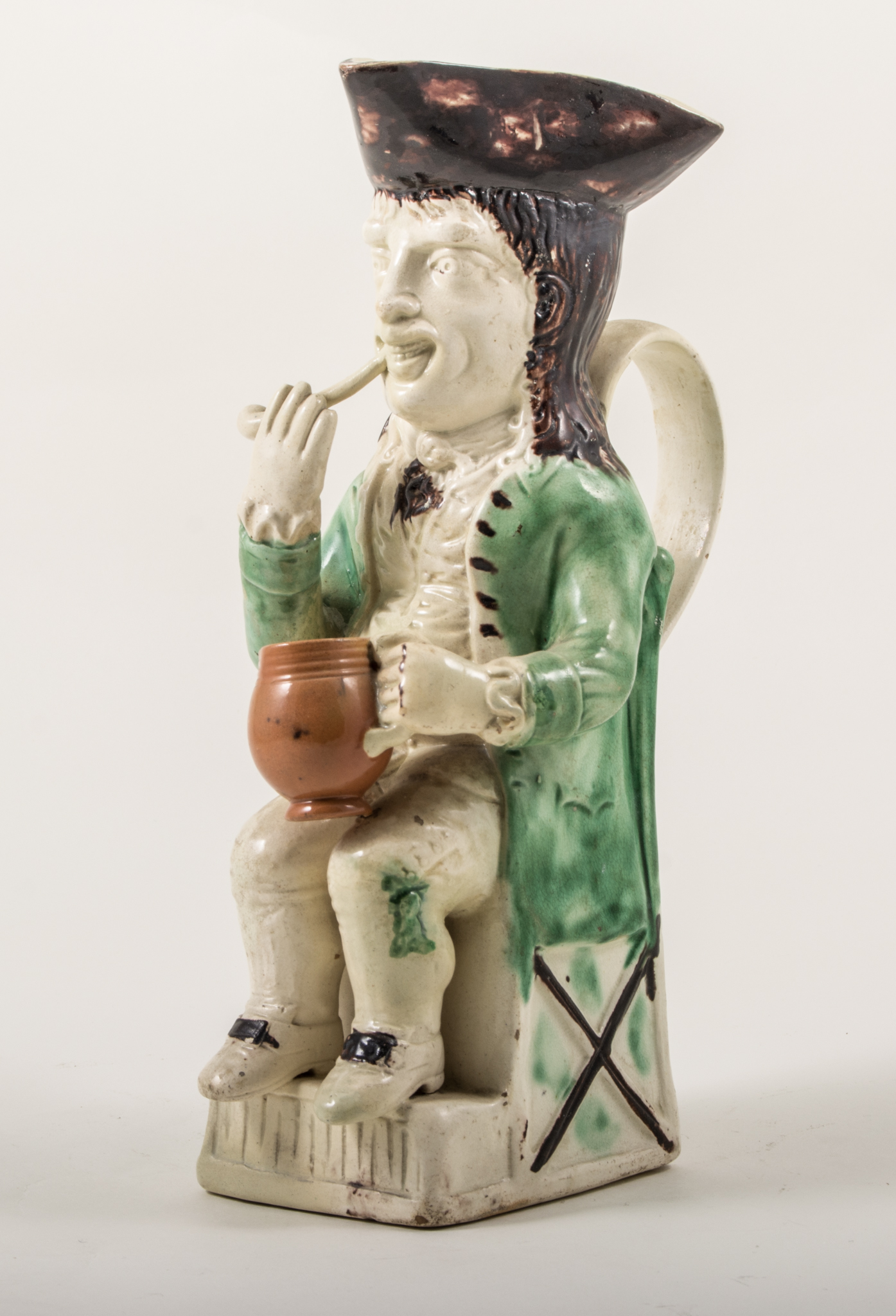 A Ralph Wood type Toby jug, Staffordshire, probably late 18th century, a slender figure seated,