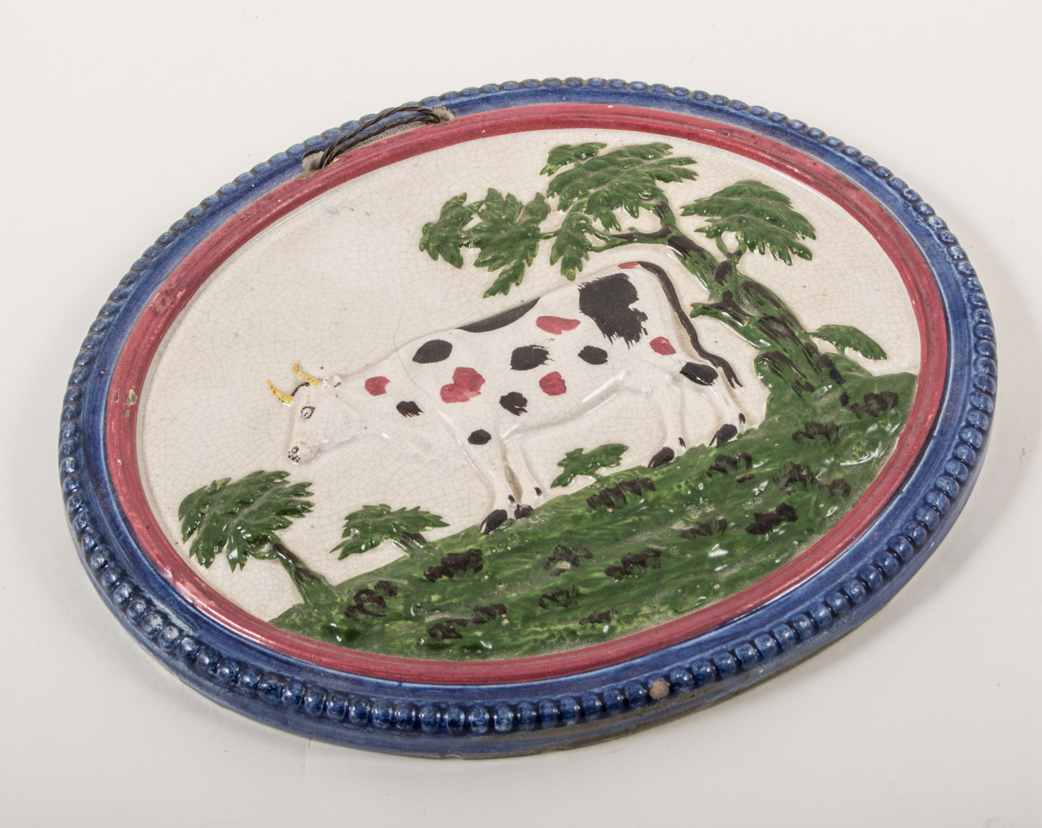 An earthenware cow in a landscape oval plaque, circa 1820, beaded and moulded surround,