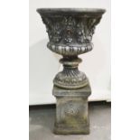 Composition stone urn with classical mask and swag design, raised on a square sectional plinth.