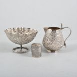 A white metal cream jug and sugar bowl, heavily embossed with flowers and scrolls,