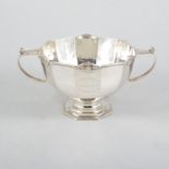 A silver twin handled pedestal bowl, plain polished twelve sided body with a reed and scroll border,