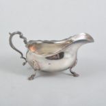 A silver sauce boat, plain cut edge design with scroll handle on three hoof and shell feet,