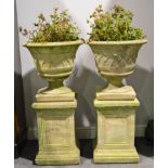 Two composite stone garden urns, raised on square block plinths.