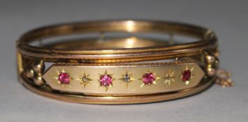 A late Victorian 9ct gold, ruby and diamond set hinged openwork bangle.