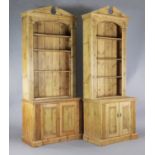 A near pair of classical style pine open bookcases, with broken arch pediments,
