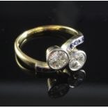 An 18ct gold and two stone diamond cross-over ring with square cut sapphire set shoulders, each