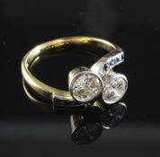 An 18ct gold and two stone diamond cross-over ring with square cut sapphire set shoulders, each