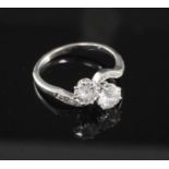 A platinum and two stone diamond crossover ring with diamond set shoulders, the tow round cut stones