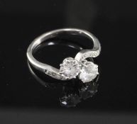 A platinum and two stone diamond crossover ring with diamond set shoulders, the tow round cut stones