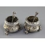 An ornate pair of Victorian silver tub shaped salts and spoons by F.B. Thomas & Co, embossed with