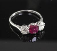 A mid 20th century platinum, ruby and diamond three stone ring, the oval cushion cut ruby flanked by