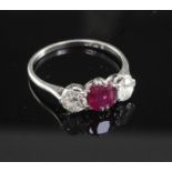 A mid 20th century platinum, ruby and diamond three stone ring, the oval cushion cut ruby flanked by