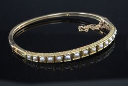 An Edwardian gold and graduated split pearl set hinged bangle, with engraved setting, in fitted