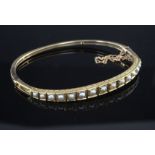 An Edwardian gold and graduated split pearl set hinged bangle, with engraved setting, in fitted