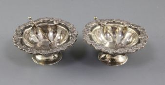 A pair of late 19th century Russian? silver circular salts with two spoons, with foliate rims, one