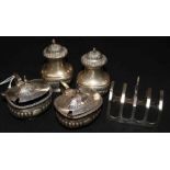 Four silver condiments and a silver toast rack.