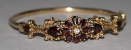 An 18ct gold garnet and diamond cluster set hinged bangle.