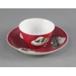 A Chinese ruby ground teabowl and saucer, 18th or 19th century, painted in famille rose enamels with