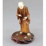 A Japanese ivory and boxwood okimono of a man, early 20th century, in standing pose, on a hardwood