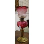 A cranberry glass oil lamp with cranberry shade and two others, smaller with shades