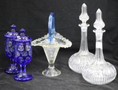 A pair of overlay lidded pots, a pair of decanters and blue handled glass basket