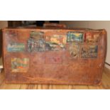 An early 20th century pigskin suitcase, decorated with travel labels, and another suitcase