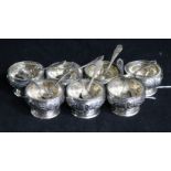 A set of seven German circular silver pedestal salts, embossed with scrolls and foliage (replacement
