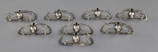 A set of eight Edwardian novelty silver menu holders modelled as fox masks on crossed riding