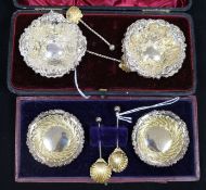 A pair of embossed silver-gilt salts with shell spoons and a similar set of fluted salts, both