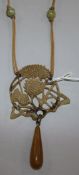 A horn drop pendant carved with a thistle and signed Cis?, on a fabric necklace with six beads.