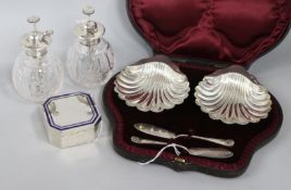 A pair of silver shell butter dishes and knives (cased), an enamel-banded silver box and a pair of