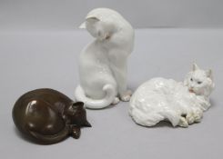 Two porcelain cats and one resin