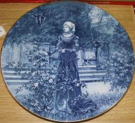 A blue-glazed circular ceramic wall plaque depicting a medieval lady in a garden, Dia 16in approx