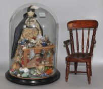 A Regency painted wood doll and accessories under glass dome and a miniature chair