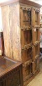 An Indian hardwood narrow cupboard, fitted panelled doors decorated with brass bosses and chain